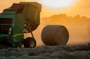 A freshly packed hay bale sites next to a tractor in a field.